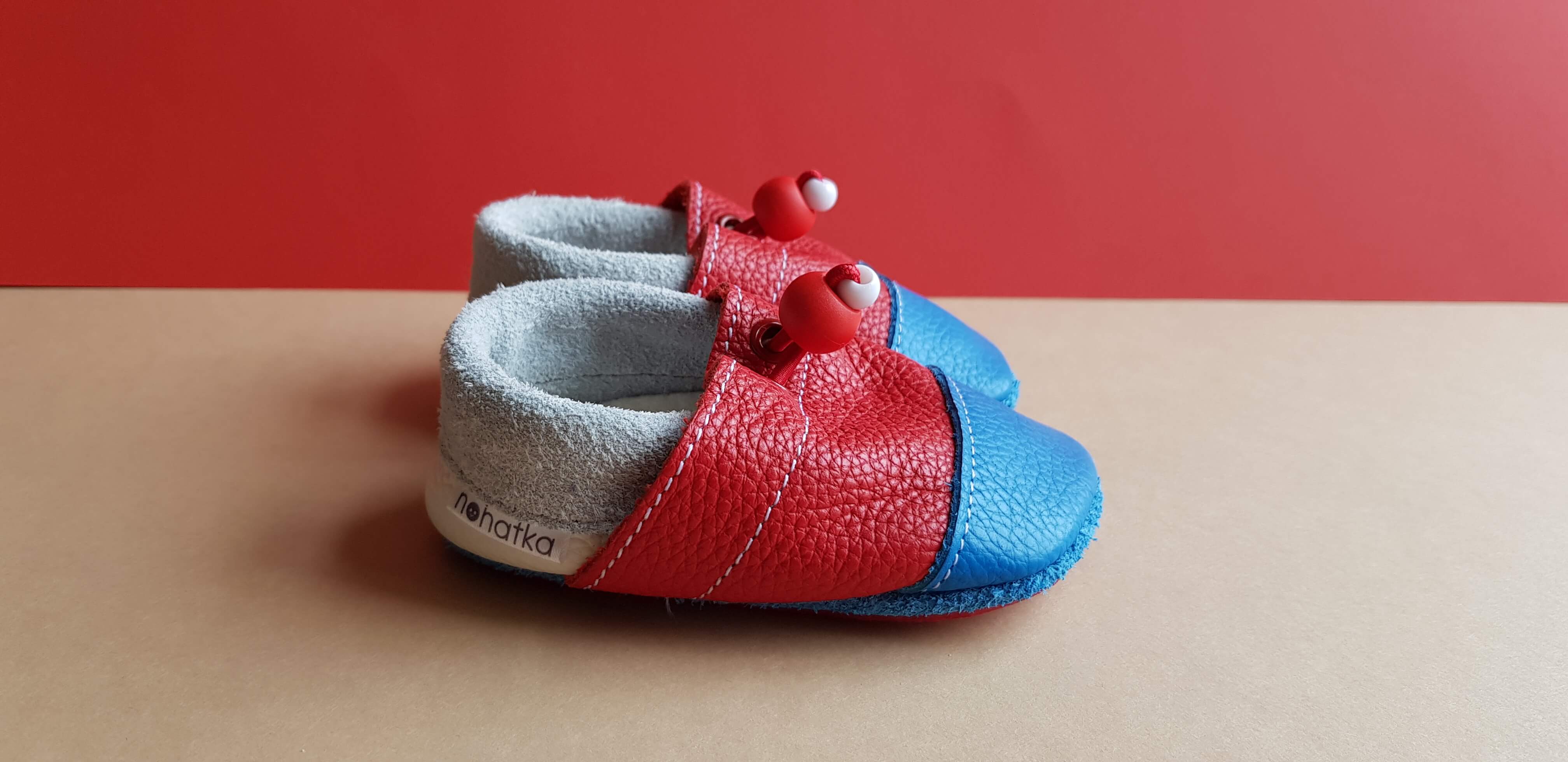 Red, Blue and White Nohatka soft sole booties/slippers for babies and toddler, anatomically shaped from soft leather with adjustable ankle fastening and anti slip indoor/outdoor sole